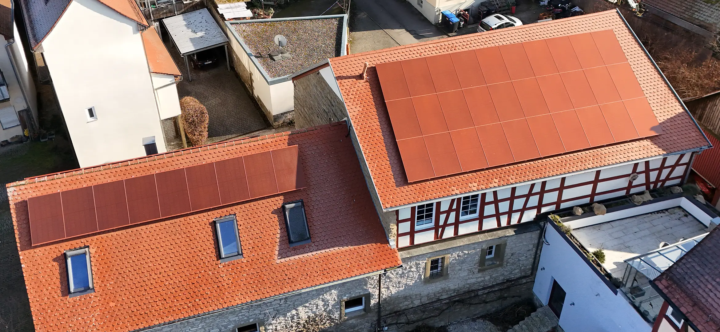 Drohnenaufnahme eines Fachwerkhauses mit roter Photovoltaikanlage auf dem Dach.
