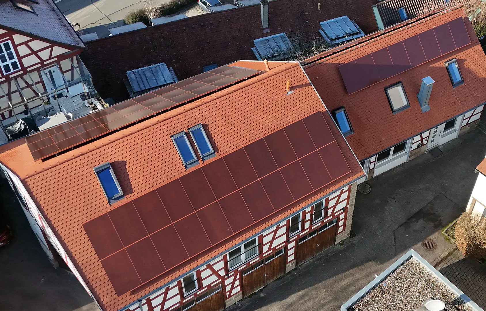 Luftaufnahme mehrerer Fachwerkgebäude mit integrierten roten Solarmodulen auf den Dächern.